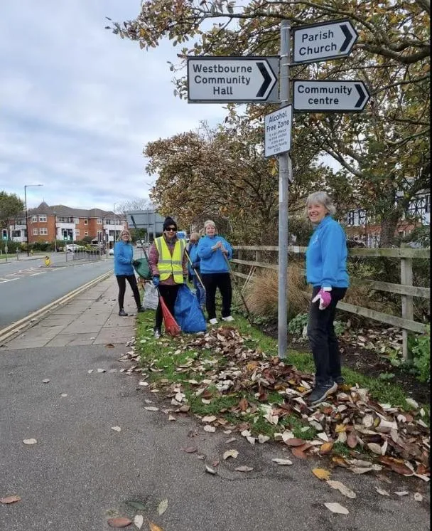 Volunteers in blue tops clearing leaves beside a West Kirby signpost